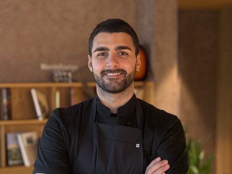 Lächelnder junger Mann mit Tattoo und schwarzer Schürze in einem Café