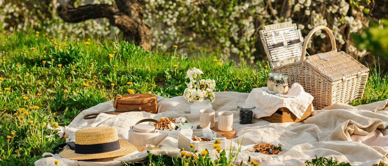 Picknicken in der Nähe des Hotel Lamm in Kastelruth – los! Picknick mit Korb, Hut und Snacks auf einer Wiese mit blühenden Bäumen