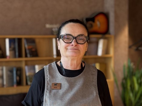Mitarbeiterin mit Brille und Schürze vor einem Bücherregal