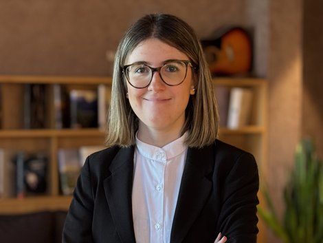Frau in Brille und Business-Kleidung steht mit verschränkten Armen vor Bücherregal