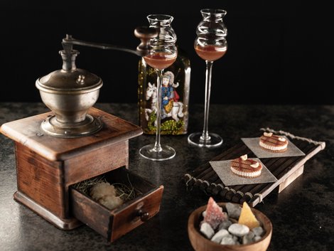 Vintage-Kaffeemühle mit Likörgläsern, Flasche, Gebäck und Schale mit Süßigkeiten
