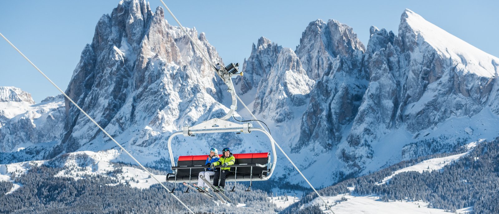 Zwei Skifahrer auf einem Skilift vor verschneiten Bergen