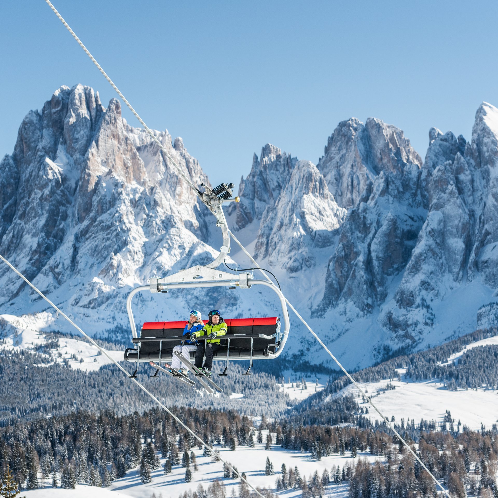 Zwei Skifahrer auf einem Skilift vor verschneiten Bergen