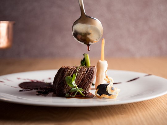 News aus unserem Hotel in Kastelruth Fein angerichteter Fleischgang mit Sauce, Spargel und Gemüse auf weißem Teller