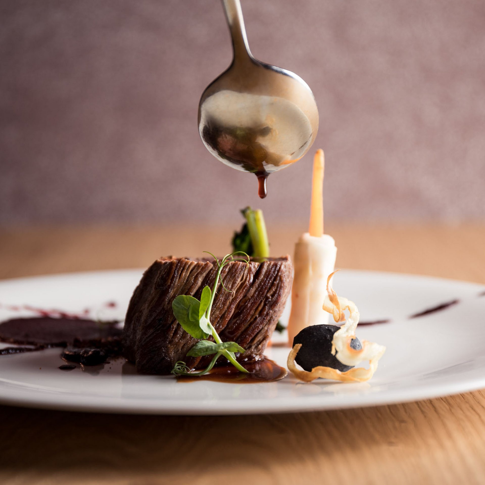 4-Sterne-Hotel Lamm am Fuße der Seiser Alm Fein angerichteter Fleischgang mit Sauce, Spargel und Gemüse auf weißem Teller