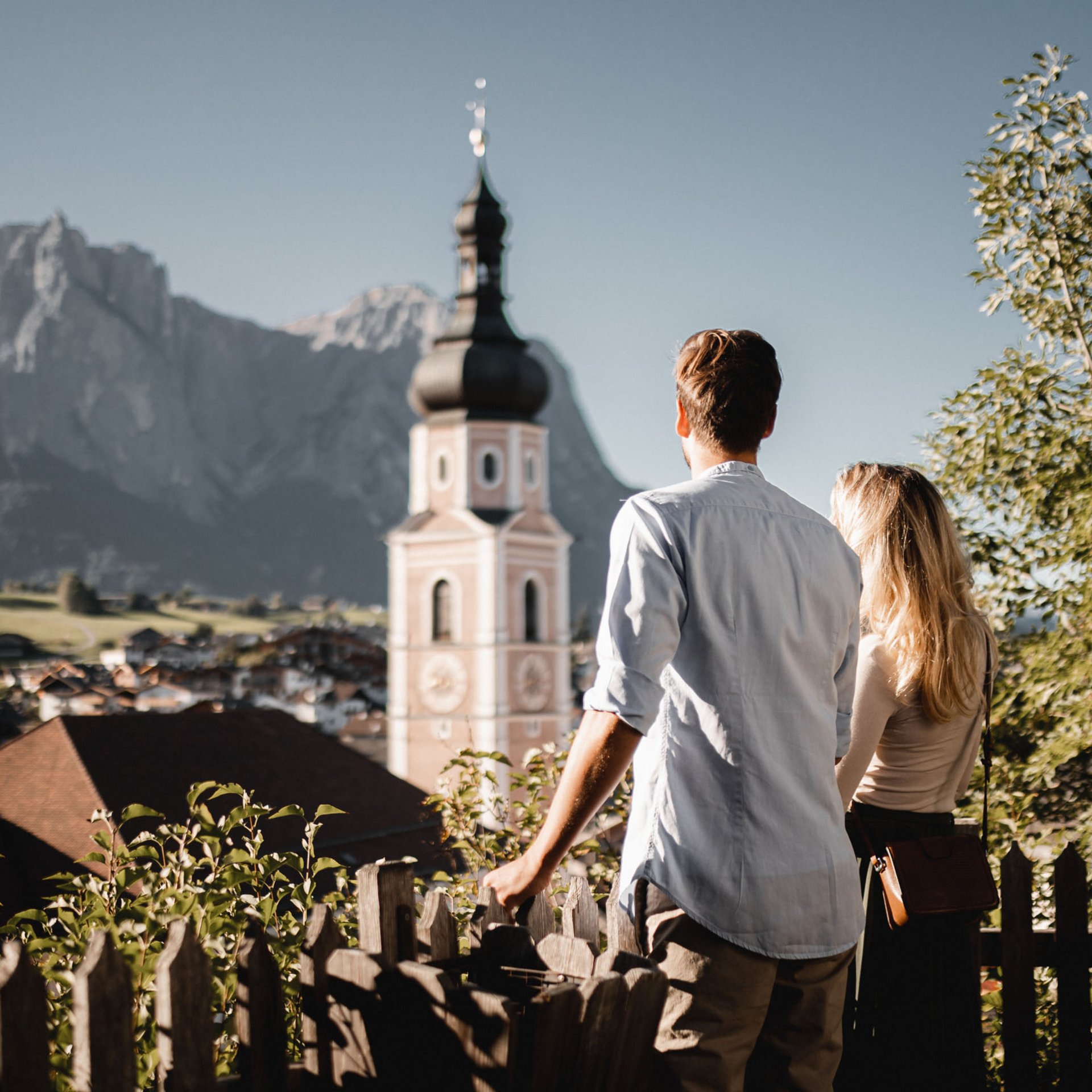 Paar blickt auf Bergkirche in malerischem Tal mit Bergen im Hintergrund