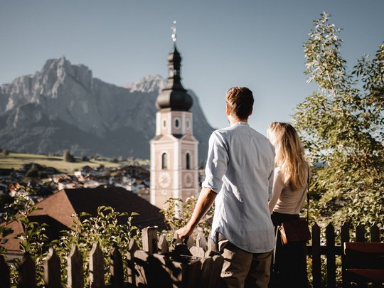 Paar blickt auf Bergkirche in malerischem Tal mit Bergen im Hintergrund
