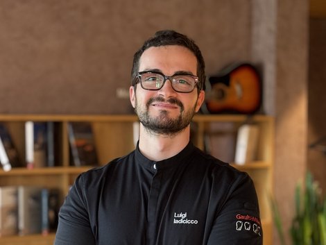 Holidays in Kastelruth at Hotel Lamm Man with glasses and black chef jacket standing in front of bookshelf and guitar
