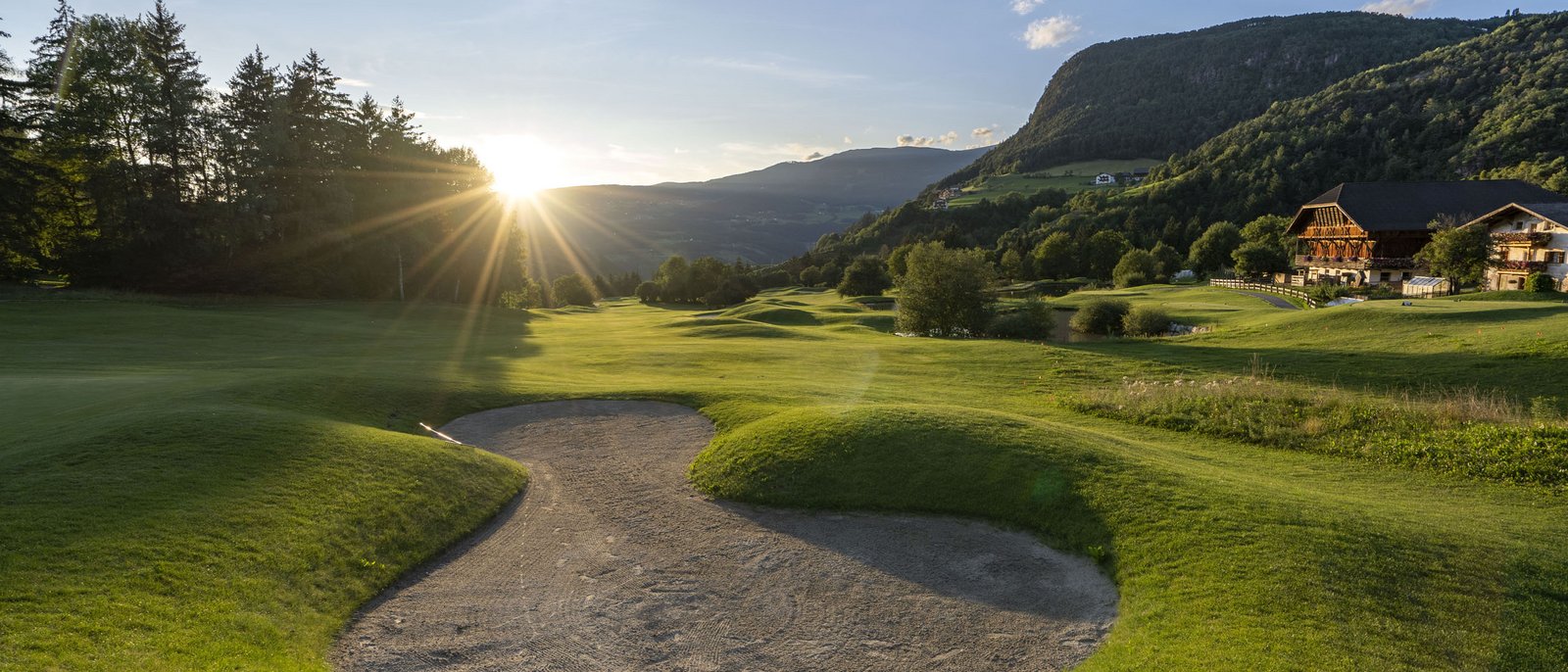 Auf zum Golfen am Fuß der Seiser Alm in den Dolomiten! Golfplatz mit Sandbunker und Sonnenuntergang in den Bergen