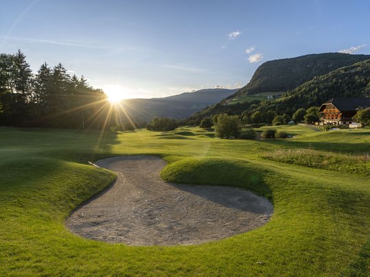 Golfplatz mit Sandbunker und Sonnenuntergang in den Bergen