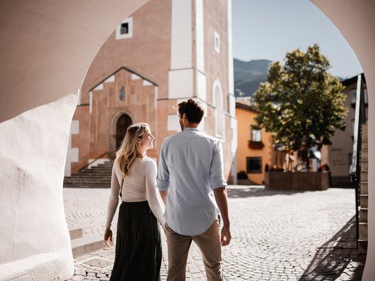 Paar spaziert durch einen sonnigen gepflasterten Platz in einer europäischen Stadt
