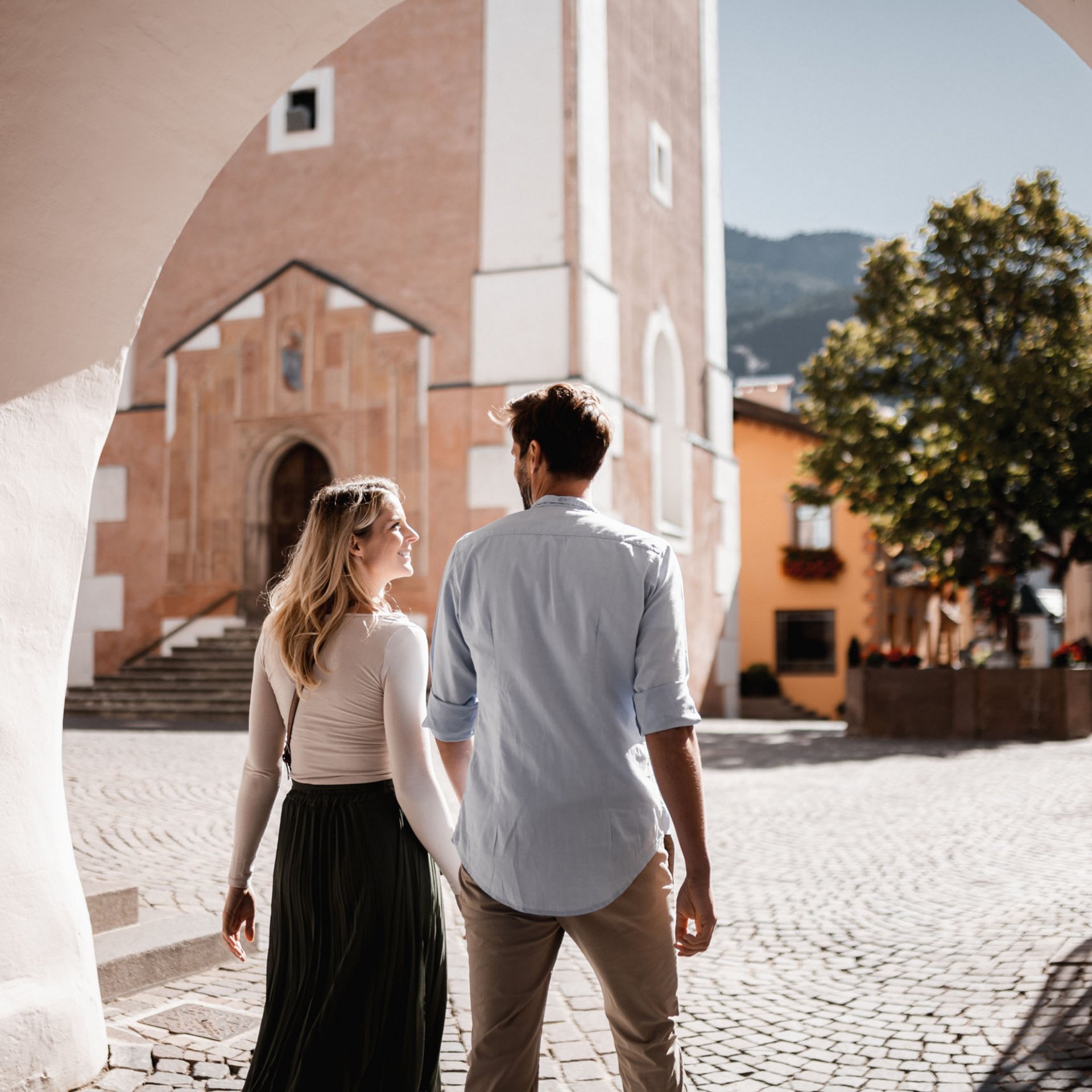 Paar spaziert durch einen sonnigen gepflasterten Platz in einer europäischen Stadt