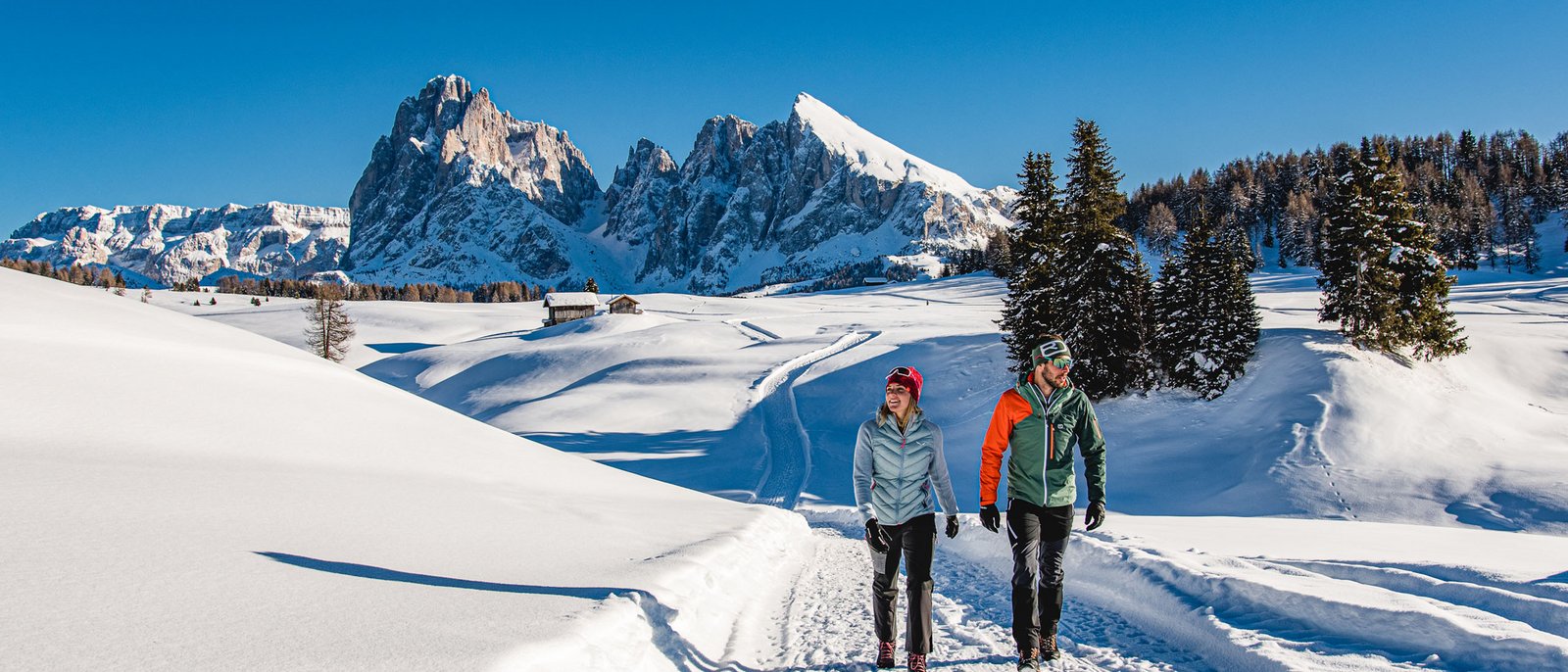 Una piccola anticipazione dell’inverno Due escursionisti camminano su sentiero innevato con montagne sullo sfondo e cielo blu